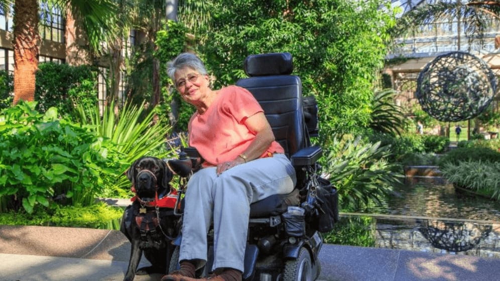 Elderly woman in a motorized wheelchair outdoors with a guide dog