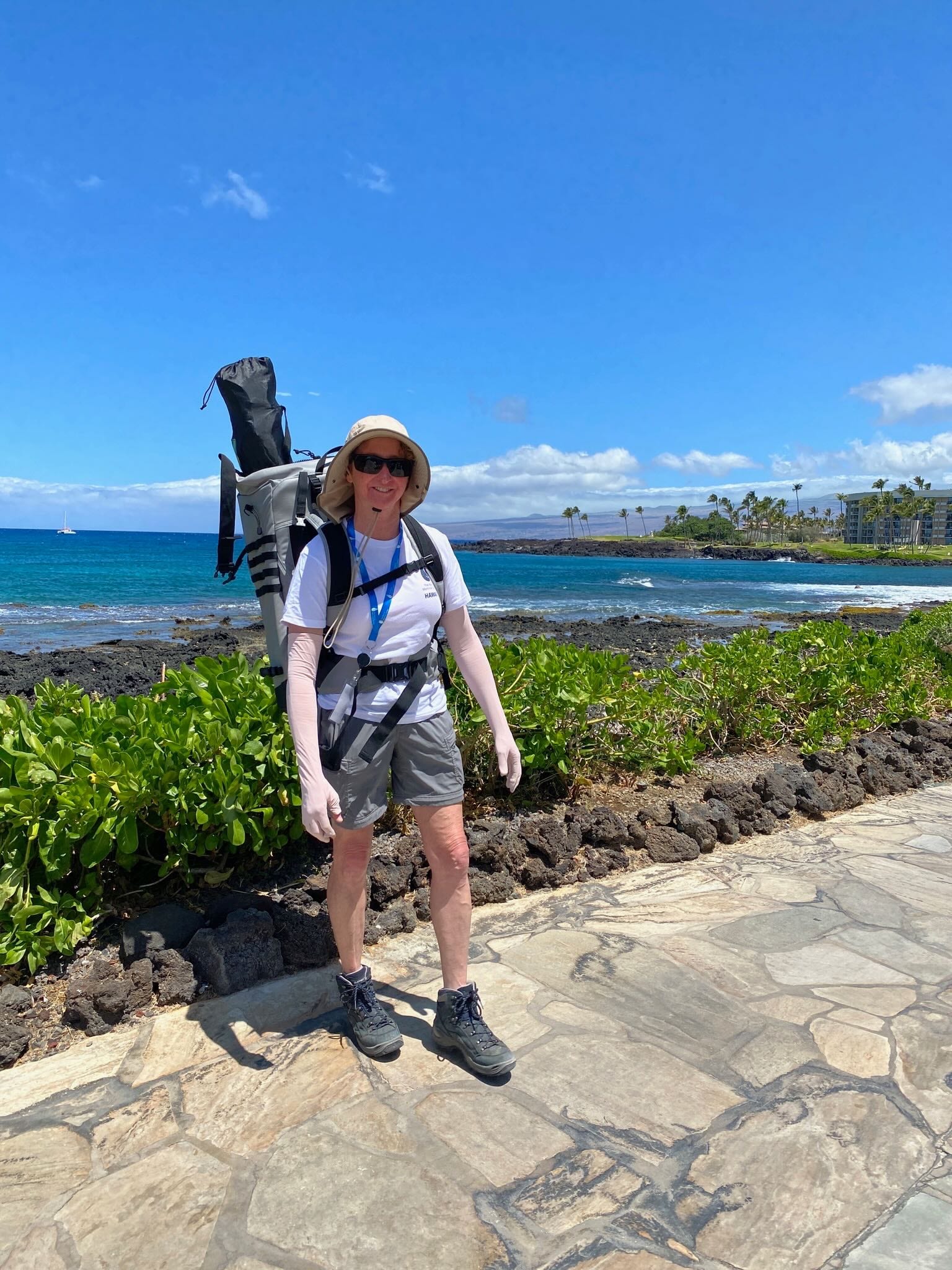 A hiker with a hydration pack on a sunny lava-rock coastal trail on the Big Island