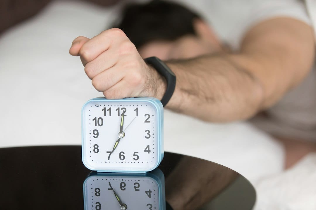 A hand pressing the top of an alarm clock beside the bed