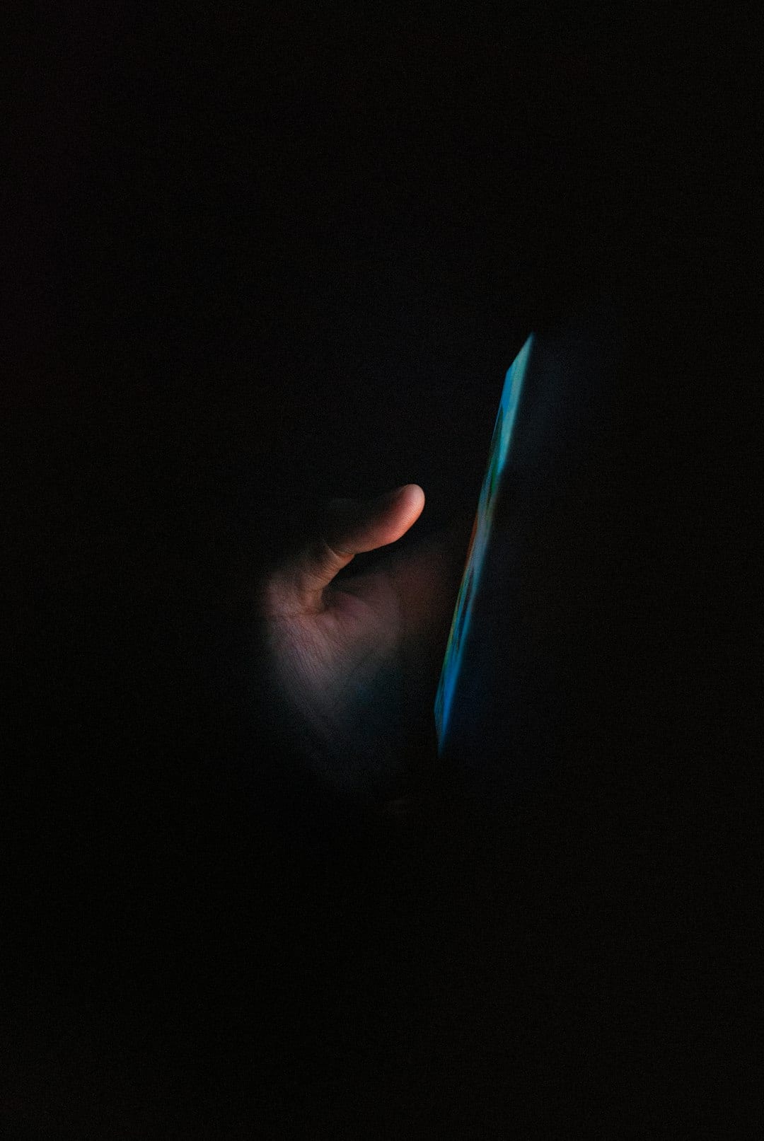 A hand holding a glowing phone in a dark room at night